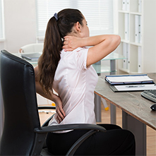 woman sitting at office desk holding neck in pain.