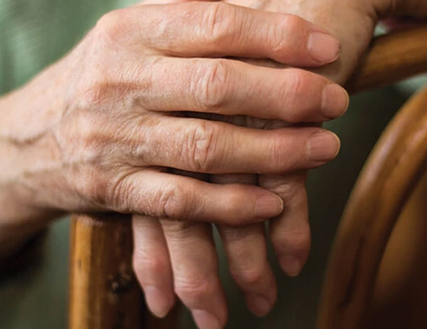 hands resting on the arm of a wooden chair