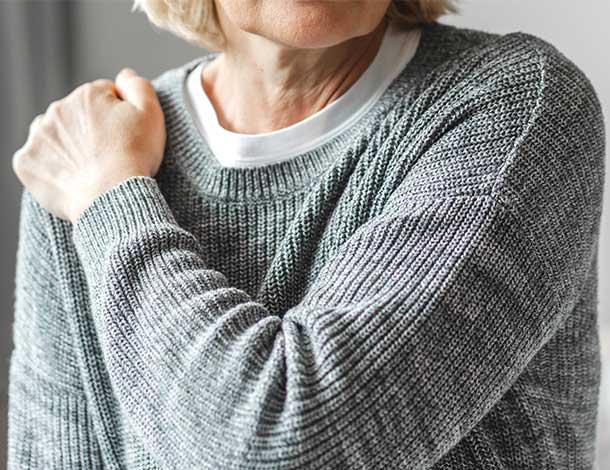 elderly woman gripping shoulder in pain